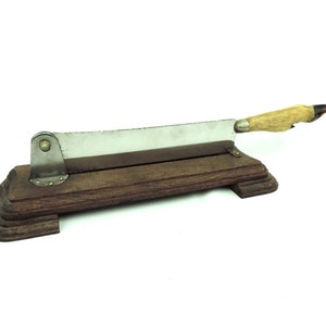 May include: A vintage silver-coloured knife with a wooden handle and a wooden base. The handle is made of a deer antler.