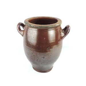 以下が含まれることがあります： 2つの小さな取っ手が付いた茶色の陶器の壺。壺は丸みを帯びたボディと広い開口部を持っています。縁は明るい茶色です。壺は、おそらく保管または装飾に使用されます。