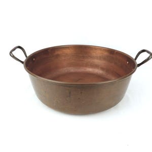 May include: A copper pot with two black metal handles. The pot is round and has a hammered finish.