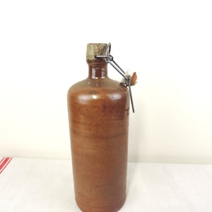 May include: A brown ceramic bottle with a cork stopper and a wire closure. The bottle has a rustic, vintage look.