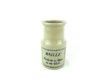 May include: A small, white ceramic jar with a blue label that reads "Maille Moutarde de Dijon au vin blanc".