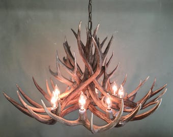 May include: A rustic chandelier crafted from intertwined antlers, featuring multiple light bulbs. The antlers are a natural brown color with lighter tips, creating a warm, inviting glow. The fixture hangs from a dark chain, suitable for a cabin or lodge.