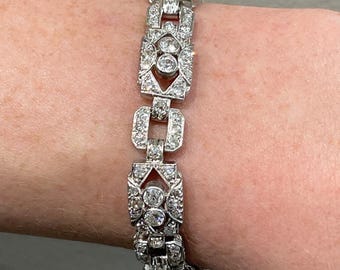 May include: A silver bracelet with a geometric design featuring a row of linked square and diamond-shaped sections, each set with sparkling clear round diamonds.