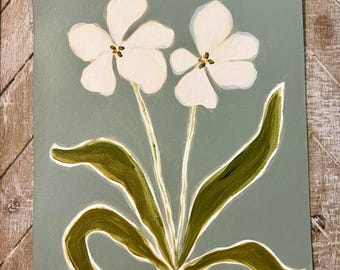 May include: A rectangular painting on a sage green background featuring two white flowers with yellow centers and long, dark olive green leaves. The stems emerge from a base with small, curly white roots, and a signature is visible in the bottom right corner.