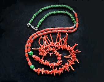 Könnte beinhalten: Eine Korallenkette mit grünen und weißen Perlen. Die Koralle ist leuchtend orangefarben und spiralförmig angeordnet. Die Kette liegt auf einem schwarzen Hintergrund.