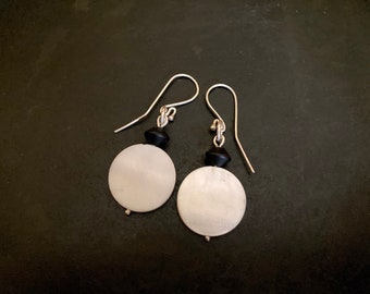 Op de afbeelding: Een paar zilveren oorhangers met witte ronde schelp kralen en zwarte ronde kralen.