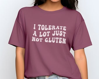 Puede incluir: Camiseta granate con el texto blanco "I TOLERATE A LOT JUST NOT GLUTEN". La camiseta de manga corta es de color liso y tiene un corte holgado.