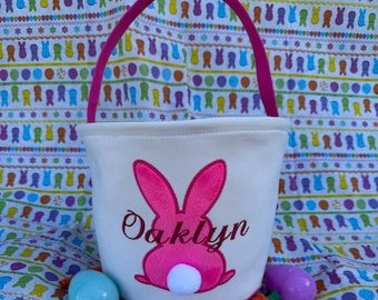 May include: White Easter basket with a pink bunny embroidered on the front. The bunny has a white fluffy tail. The basket has a pink handle and the name "Oaklyn" is embroidered below the bunny.
