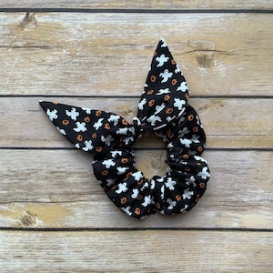 Op de afbeelding: Een zwart-witte scrunchie met een Halloween-print van geesten en pompoenen.