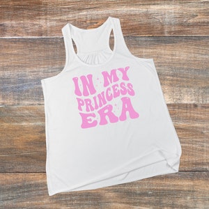 May include: White tank top with a pink graphic that says "In My Princess Era" in a retro font.