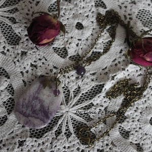 May include: A purple and white agate stone pendant necklace with a bronze chain and a small purple bead. The necklace is displayed on a white crocheted lace tablecloth.