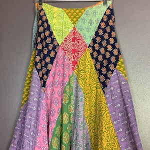 Puede incluir: Una falda de patchwork colorida con una variedad de patrones florales y geométricos en tonos de morado, rosa, verde, amarillo, azul y rojo.