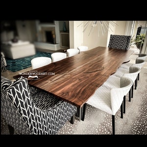 May include: A large, live edge walnut dining table with a natural wood finish. The table is surrounded by white upholstered chairs with black legs. The table is handcrafted by WonderWoodArt.com.