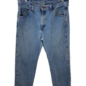 May include: A pair of light blue denim jeans hanging on a wooden hanger. The jeans have a classic five-pocket style and a straight leg.