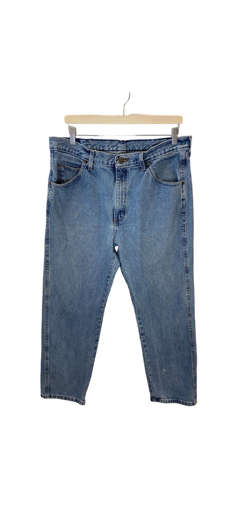 May include: A pair of light blue denim jeans hanging on a wooden hanger. The jeans have a classic five-pocket style and a straight leg.