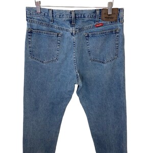 May include: A pair of light blue denim jeans with a brown leather patch that says "Wrangler" on the back pocket.