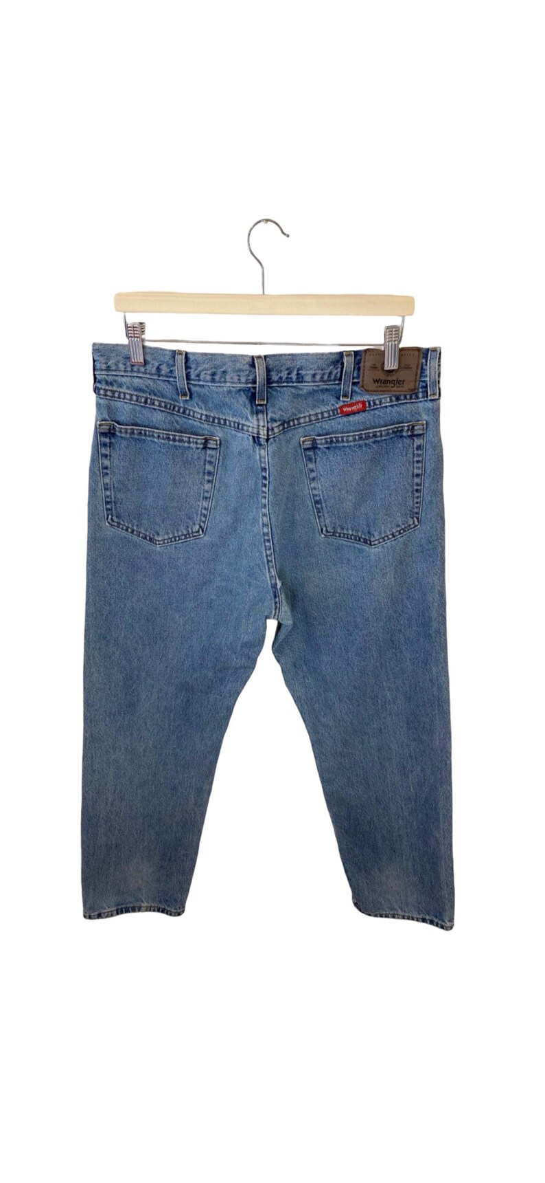 May include: A pair of light blue denim jeans with a brown leather patch that says "Wrangler" on the back pocket.