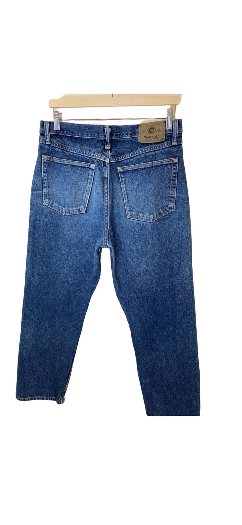 May include: A pair of blue denim jeans with a brown leather Wrangler label on the back pocket.