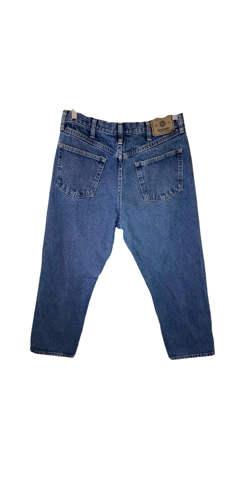 Pode incluir: Um par de cal&ccedil;as de ganga azul com um remendo de couro castanho que diz "Wrangler" no bolso de tr&aacute;s.