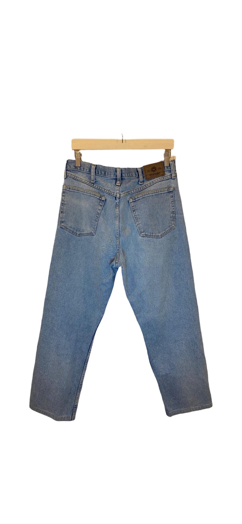 Peut inclure: Un jean en denim bleu clair avec un &eacute;cusson en cuir marron sur la poche arri&egrave;re. L'&eacute;cusson porte l'inscription "Wrangler".