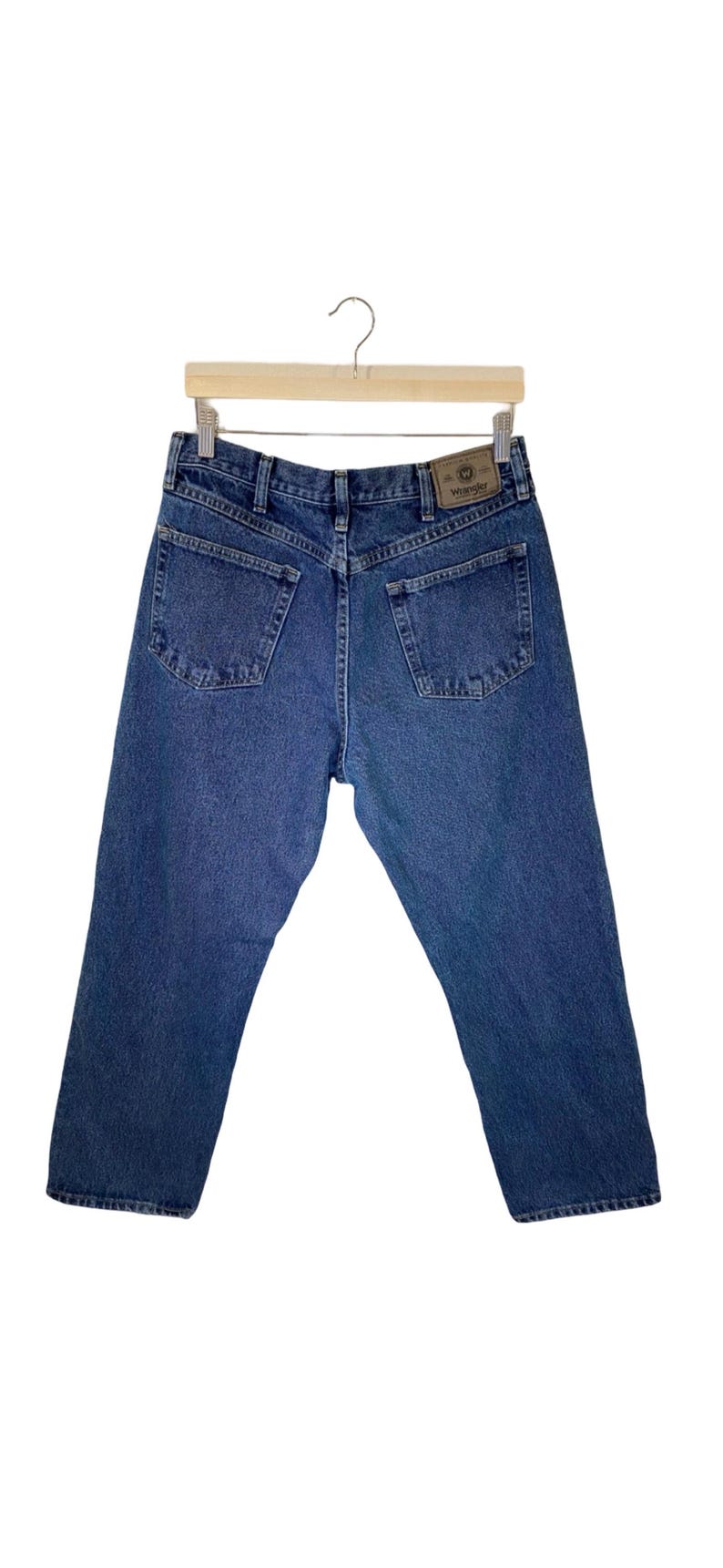 Pode incluir: Um par de cal&ccedil;as de ganga azul com um remendo de couro castanho que diz "Wrangler" nas costas.