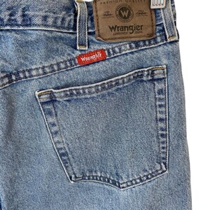 May include: A pair of light blue denim jeans with a brown leather patch that says "Wrangler Authentic Jeans" and a red patch that says "Wrangler".