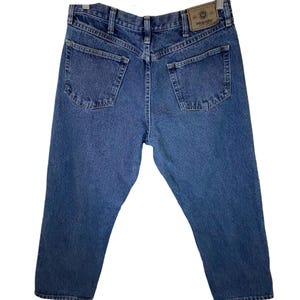 Pode incluir: Um par de cal&ccedil;as de ganga azuis com um remendo de couro castanho no bolso de tr&aacute;s que diz "Wrangler".