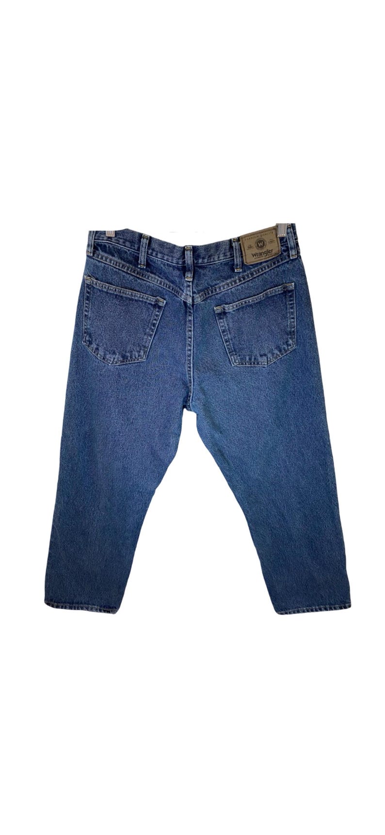 Pode incluir: Um par de cal&ccedil;as de ganga azuis com um remendo de couro castanho no bolso de tr&aacute;s que diz "Wrangler".