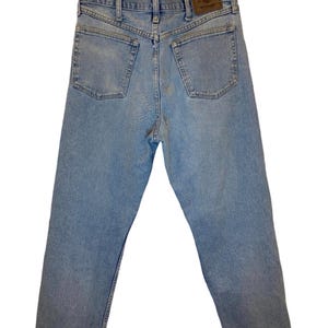 Peut inclure: Un jean en denim bleu clair avec un &eacute;cusson en cuir brun sur la poche arri&egrave;re qui dit "Wrangler".