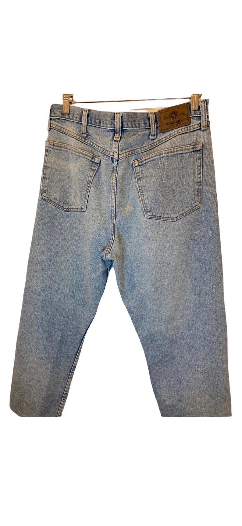 Peut inclure: Un jean en denim bleu clair avec une &eacute;tiquette Wrangler en cuir marron sur la poche arri&egrave;re.