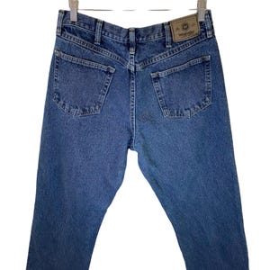 Pode incluir: Um par de cal&ccedil;as de ganga azuis com uma etiqueta Wrangler de couro castanho no bolso de tr&aacute;s.