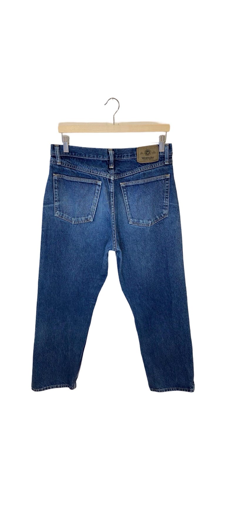 May include: A pair of blue denim jeans with a brown leather Wrangler label on the back pocket.