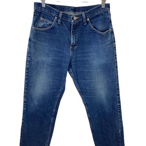 May include: A pair of blue denim jeans hanging on a wooden hanger. The jeans have a classic straight leg style and a button fly.