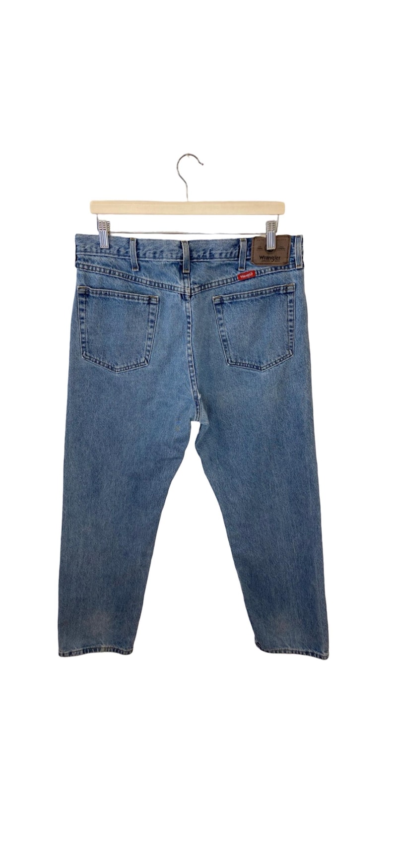May include: A pair of light blue denim jeans with a brown leather Wrangler label on the back pocket.