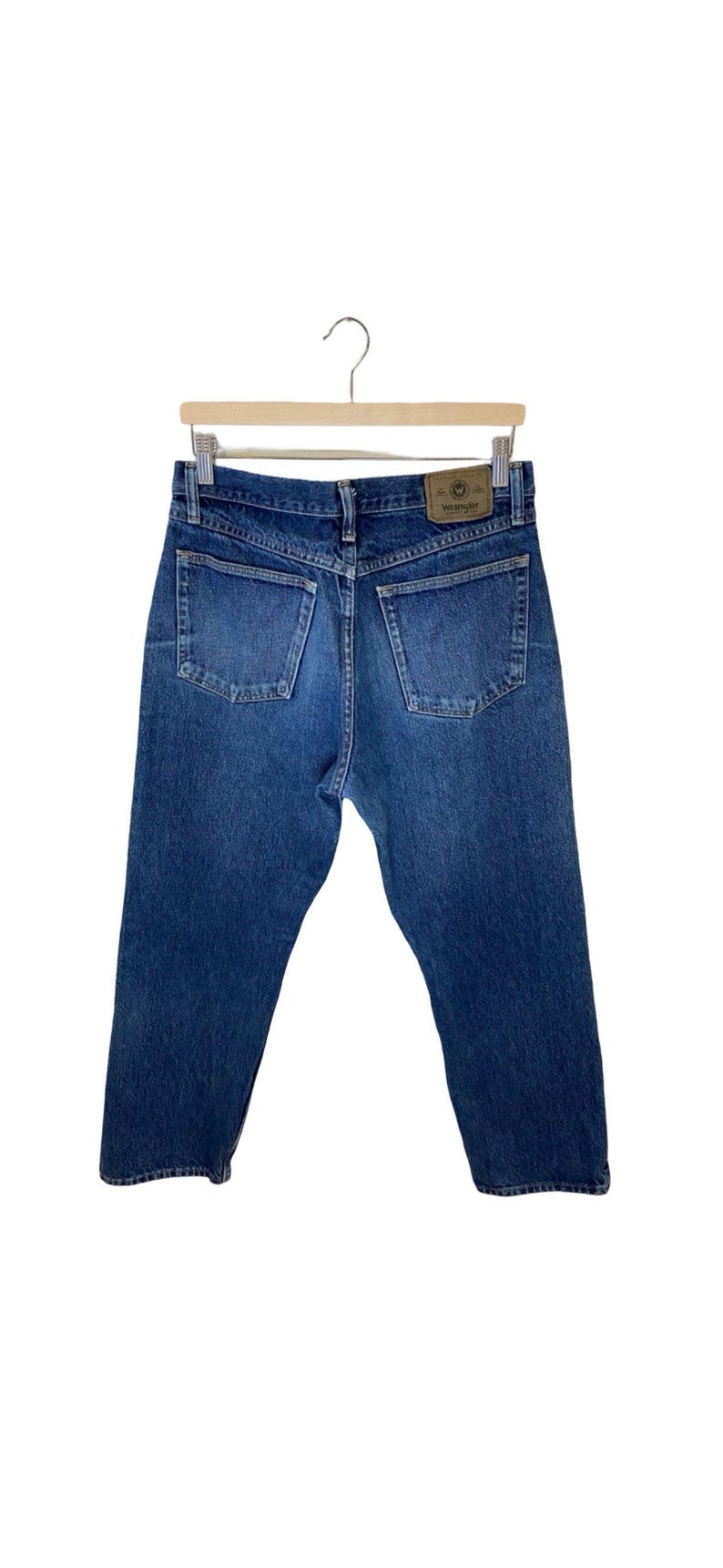 May include: A pair of blue denim jeans with a brown leather Wrangler label on the back pocket.