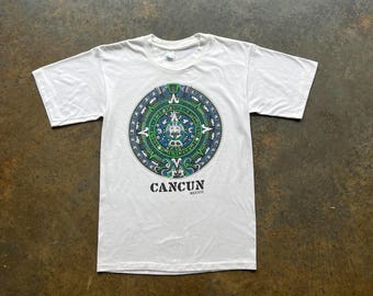 May include: White t-shirt with a green, blue, and black graphic of a Mayan calendar with the text "CANCUN MEXICO" underneath.
