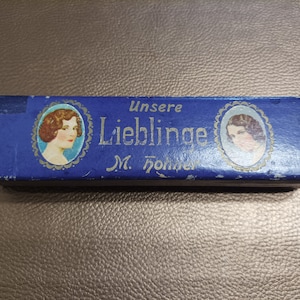 Peut inclure: Une boîte bleue avec le texte "Unsere Liebling M. Jöhrer" et deux images de femmes aux cheveux courts.