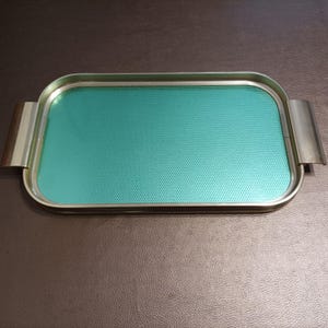 Peut inclure: Un plateau de service rectangulaire avec un cadre en métal doré et une surface texturée bleu sarcelle.
