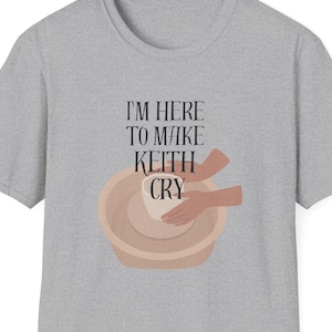 Puede incluir: Una camiseta gris jaspeada con el texto "Estoy aquí para hacer llorar a Keith" y una ilustración de manos haciendo cerámica.