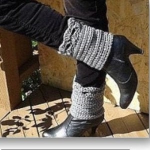 Puede incluir: Polainas de ganchillo grises. Las polainas se muestran con botas y pantalones negros. Las polainas tienen un borde festoneado y están hechas de un hilo suave y texturizado. La imagen también muestra un primer plano de las polainas.