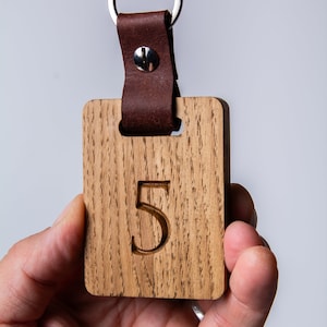 May include: A wooden keychain with a leather strap and a metal ring. The wooden tag has the number "5" engraved on it.
