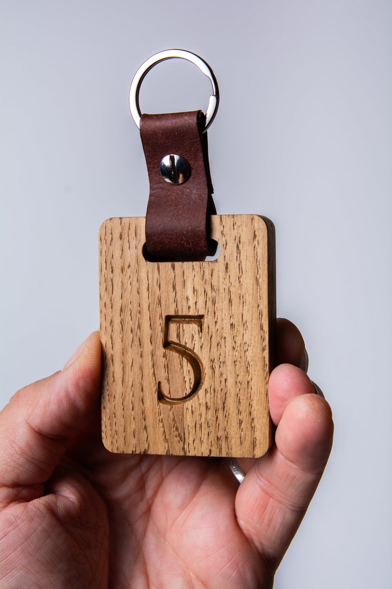 May include: A wooden keychain with a leather strap and a metal ring. The wooden tag has the number "5" engraved on it.