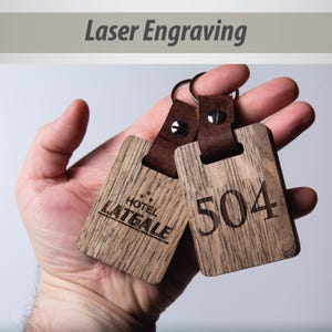 May include: Two wooden keychains with leather straps. One keychain is engraved with "HOTEL LAITGALE" and the other is engraved with "504".