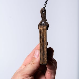 May include: A wooden keychain with a leather loop and a metal ring. The keychain is dark brown and has a wood grain pattern.