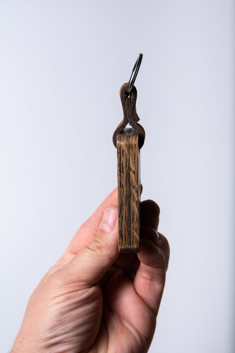 May include: A wooden keychain with a leather loop and a metal ring. The keychain is dark brown and has a wood grain pattern.
