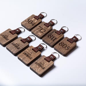May include: Eight wooden keychains with leather straps. Each keychain has a different number engraved on it, including 504, 712, 811, and 805. The keychains also have the words "Hotel Latgale" engraved on them.