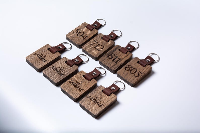 May include: Eight wooden keychains with leather straps. Each keychain has a different number engraved on it, including 504, 712, 811, and 805. The keychains also have the words "Hotel Latgale" engraved on them.