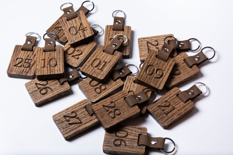 May include: A pile of wooden keychains with leather straps and metal rings. Each keychain has a number engraved on it, ranging from 01 to 28.