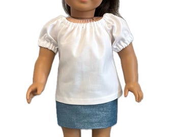 May include: A doll with brown hair and bangs wearing a white short-sleeved blouse with an elasticized neckline and sleeves, paired with a blue denim-style mini skirt. The doll has brown eyes and a neutral expression, standing in a front-facing pose.