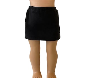 May include: A black skirt made of a soft fabric. The skirt is designed to fit a doll. The skirt has an elastic waistband and is knee-length. The skirt is a solid black color.